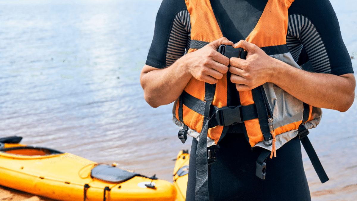 male kayaker wearing a wetsuit and putting on a pfd