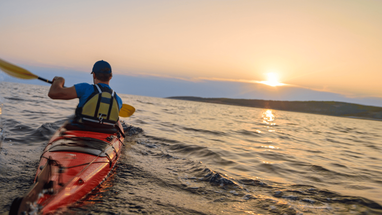 man paddling a kayak into a sunset