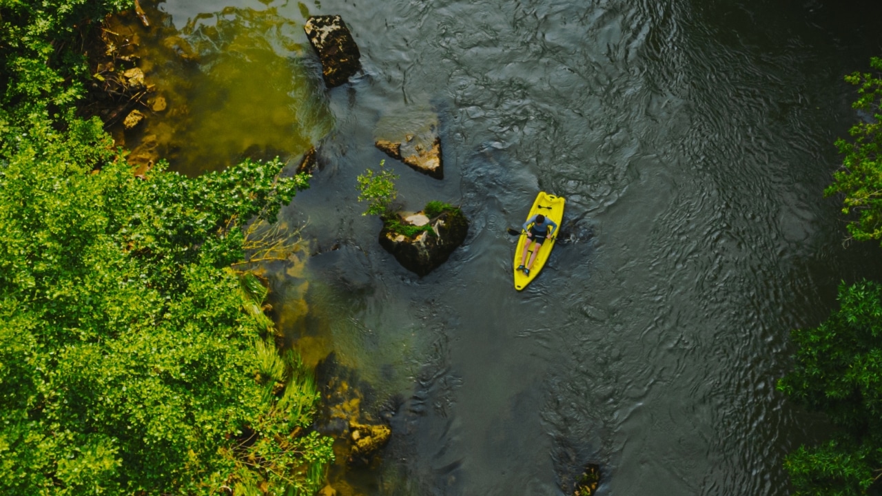 Birds-eye view of a woman paddling a yellow kayak on a river